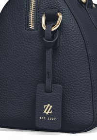 Navyblauwe leren handtas met structuur en gouden hardware, met een rits sluiting en een rechthoekig label waarin "EST. 2007." is gedrukt.