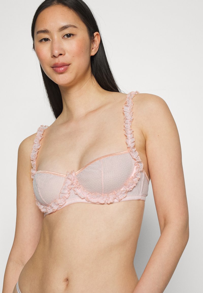 Sutiã em rosa claro com borda de renda rendada ao longo das extremidades e alças, apresentando um padrão texturizado e suporte de aros.