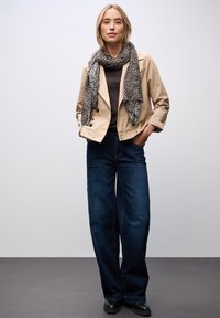 Giacca beige corta, top marrone scuro, jeans scuri a gamba larga e una sciarpa maculata nera e beige, con una texture di tessuto liscia.