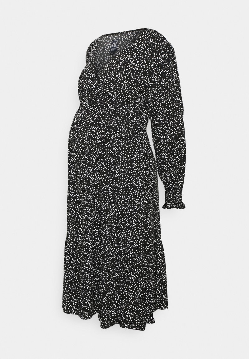 Sort graviditetskjole med hvidt blomsterprint, lange ærmer, V-hals og indsamlet taljepanel designet til komfort under graviditet.