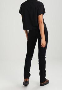 Lyhythihainen musta cropped t-paita yhdistettynä slim-fit mustiin farkkuihin. Asukokonaisuutta täydentävät ruskeat kengät ja yksinkertainen tausta.