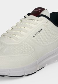 Baskets blanches texturées Tommy Hilfiger avec lacets blancs, doublure intérieure noire et patch logo bordeaux sur la languette.