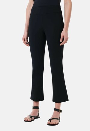 Leggings neri a vita alta, cropped e con orlo svasato, realizzati in un materiale elasticizzato. Indossati con sandali neri piatti.