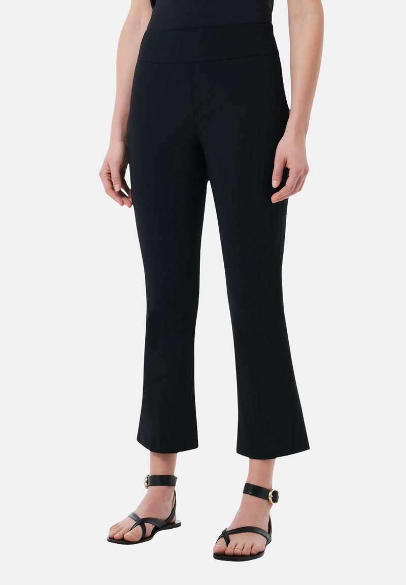 Leggings neri a vita alta, cropped e con orlo svasato, realizzati in un materiale elasticizzato. Indossati con sandali neri piatti.