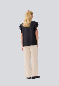 Black short-sleeve top with ruffled accents, paired with textured light beige wide-leg pants. Black shoes visible at the bottom.