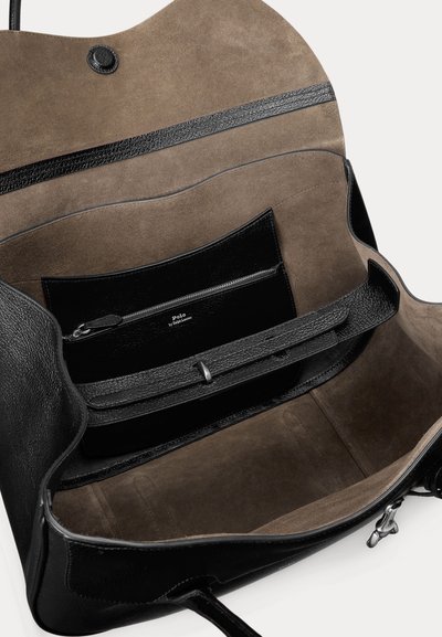 Bolso abierto de cuero negro que muestra el interior de ante marrón con un bolsillo con cremallera etiquetado como Polo by Ralph Lauren y una correa ajustable en el interior.