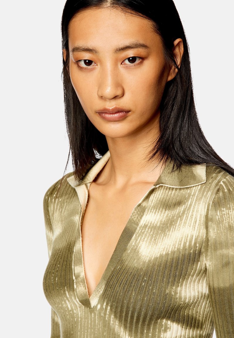 Top côtelé vert olive avec un décolleté en V profond et un col. Le tissu a une texture brillante avec des stries plus claires subtiles et une coupe ajustée.