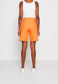 Oranžové šortky s půvabným střihem, s pasem střední výšky, rovnými nohavicemi a dvěma zadními kapsami. V kombinaci s bílými teniskami.
