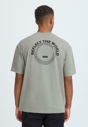 Grå bomulds t-shirt med korte ærmer. Bagsiden har en cirkulær grafik med teksten "REFLECT THE WORLD" og året "1993" i midten.