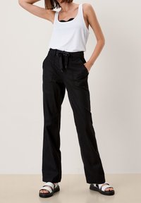 Pantalon noir taille haute avec cordon de serrage, doté de poches avant et d'une coupe ample, porté avec un débardeur blanc et des sandales noires.