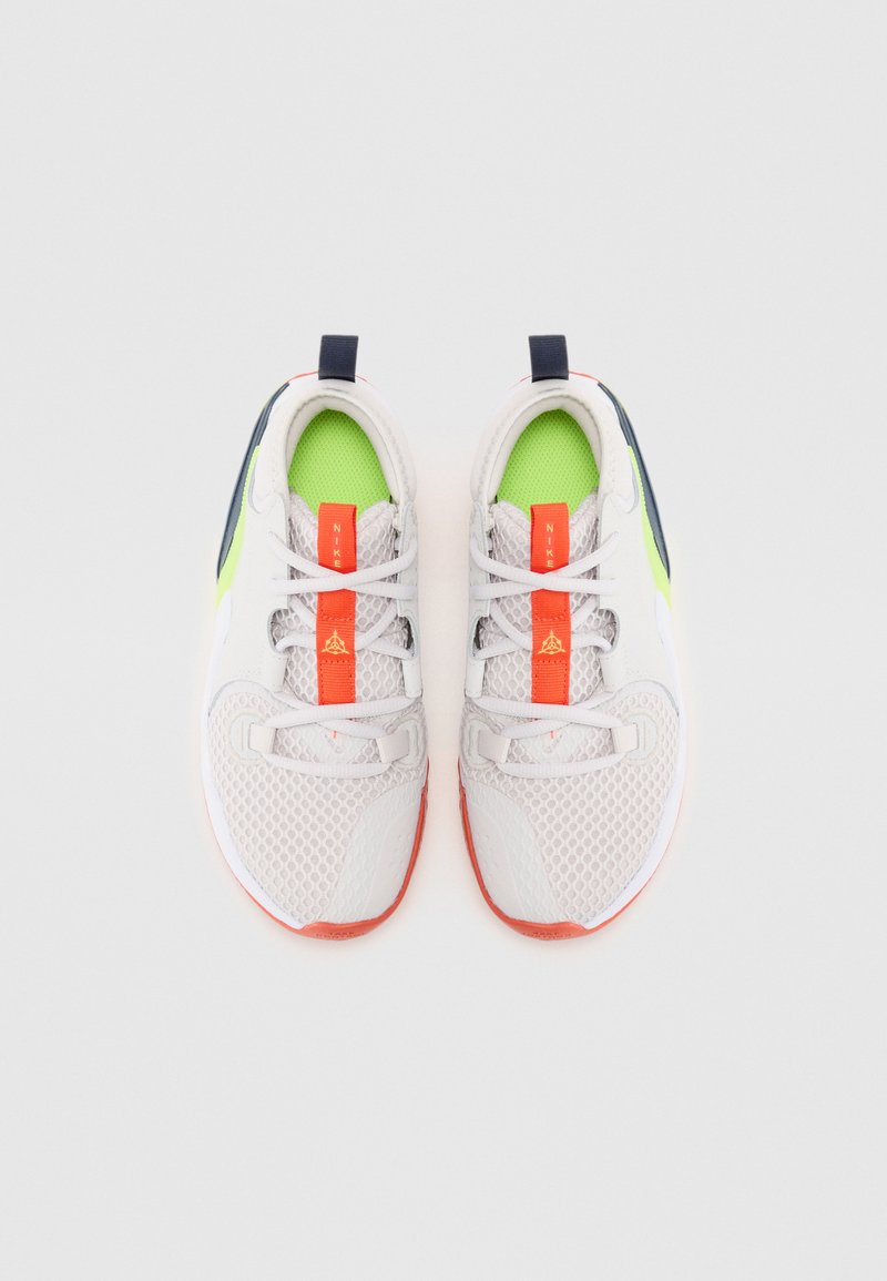 Zapatillas deportivas blancas y grises con parte superior de malla, detalles en verde neón, cordones naranjas y suela texturizada; incluye una lengüeta y un logo.