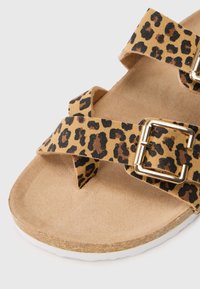 Σανδάλι με λεοπάρ μοτίβο και διασταυρούμενες λωρίδες από μαλακό ύφασμα, με μεταλλική χρυσή πόρπη. Καφέ σόλα με λευκή άκρη.