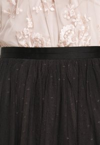 Jupe en tulle noire avec une ceinture en satin, un design superposé et une texture subtile avec de petits points décoratifs partout.