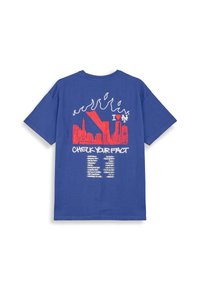 Camiseta de algodón azul con mangas cortas. La parte trasera presenta un diseño gráfico en rojo de un horizonte de ciudad, llamas y un texto que dice "REVISA TUS HECHOS."