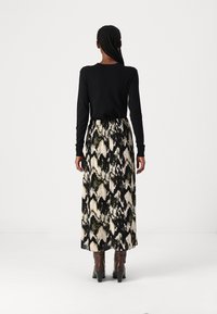 Zwarte langmouwtop gecombineerd met een lange, gemusterde rok in zwart, crème en olijfgroen. Bruine hoge laarzen maken de look af.