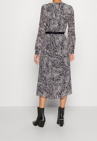 Vestido de manga larga en estampado de cebra en blanco y negro, con cintura ceñida, tela fluida y un dobladillo de longitud media. Combinado con botas de tacón negras.