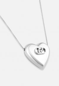 Ezüst szív alakú medál nyaklánc, kulcslyuk díszítéssel, vékony láncról felfüggesztve. Simább textúra, fényes felület, minimalista dizájn.