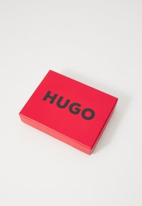 Red rectangular box with a glossy finish, featuring the bold black text "HUGO" on the top. No additional patterns or accents visible.