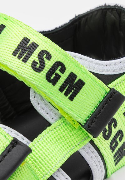 Sandálias pretas com largas tiras neon verdes com "MSGM" impresso em preto. Os detalhes incluem acabamentos cinzas e uma superfície texturizada.