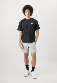 Must värviline T-särk lühikeste varrukatega valge logo, hallid lühikesed püksid, mustad sokid ja valged spordij jalanõud. Riietus on juhuslik ja sportlik.
