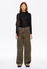 Czarna bluzka z długim rękawem z drapowanym wzorem, oliwkowozielone spodnie o szerokich nogawkach z fakturowanym wzorem oraz beżowe buty z czarną podeszwą i sznurowadłami.