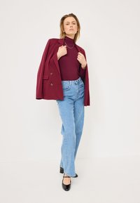 Burgundy double-breasted blazer over a fitted burgundy turtleneck, paired with light blue high-waisted jeans and black heeled shoes.