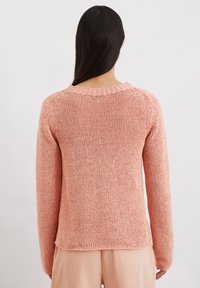 Pull en tricot doux couleur pêche avec des manches longues, un col ras-du-cou et un design en mailles texturées et lâches. Pas de fermetures visibles.