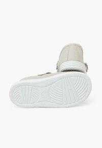 Zapatos beiges con parte superior de cuero suave y suela de goma blanca. Cuentan con una correa de velcro y suturas sutiles.