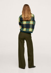 Sweter w niebiesko-zieloną kratę z długimi rękawami; zestawiony z oliwkowozielonymi, szerokimi spodniami z wysokim stanem.