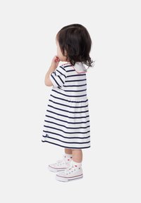 Gestreiftes Kleid in Weiß und Marineblau mit kurzen Ärmeln, einem runden Kragen mit rotem Saum, kombiniert mit weißen Sneakers und Socken mit Herzmuster.