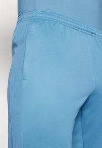 Pantalones deportivos de color azul claro, confeccionados en una tela suave, que presentan un panel de malla, cinturilla elástica y detalle de bolsillo lateral.
