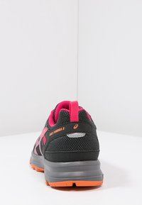 Chaussure de course noire et rose avec tige en mesh, col rembourré et semelle en caoutchouc. Présente des accents gris et une semelle extérieure orange. Modèle : Trail-Tambora 5.