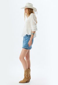 Blusa blanca, ligera, con peplum y mangas largas; combinada con pantalones cortos de mezclilla desgastados y botas de vaquero marrones con costura decorativa.