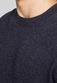 Pull bleu marine à col rond, fabriqué à partir d'un tissu doux et texturé. Le col et les poignets côtelés ajoutent une touche subtile au design.