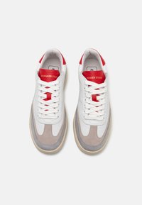 Hvite lær sneakers med grå semsket skinn-detaljer, rød lær hæl og hvite snørebånd. Har en avrundet tå og teksturert gummisåle.