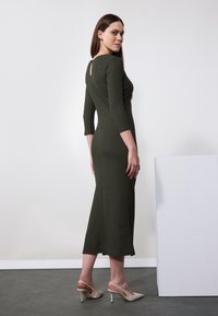 Olivgrön ribbad klänning med trekvartslånga ärmar och en nyckelhålsknapp bak. Modellen har kombinerat den med nude slingback-hälar.