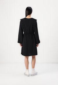 Black dress with long sleeves, lace detailing on shoulders, elastic waist, and a relaxed fit, paired with white high-top sneakers.