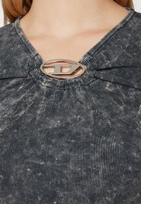 Grå ribbad topp med v-ringning, som har en knytdesign centrerad med en silver ovala hårdvaruaccents. Subtilt sliten textur.