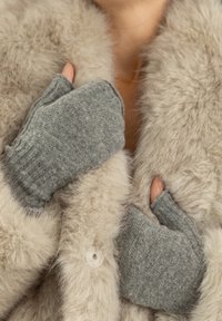 Szare rękawiczki bez palców wykonane z miękkiej dzianiny, trzymane przy beżowym futrzanym płaszczu o puszystej fakturze i z guzikiem.