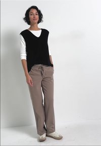 Svart ärmlös topp över en vit långärmad skjorta; beige lösa byxor; låga sneakers; neutral färgpalett; avslappnad passform.
