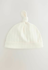Bonnet en coton côtelé blanc avec un sommet noué, doté d'une texture douce et d'un revers replié. Subtiles rayures roses claires visibles dans le tissu.