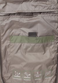 Wasserabweisender und winddichter Stoff in einem hellen Braunton, ausgestattet mit einer grünen Akzenttasche und Nachhaltigkeitsetiketten.