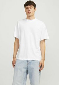 Hvid bomulds t-shirt med korte ærmer, rund hals og afslappet pasform, parret med lyseblå denim jeans. Minimalistisk design, ingen mønstre.