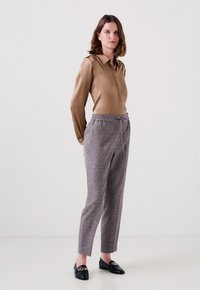 Bruine satijnen blouse met kraag, grijze textuurbroek met elastische taille, en zwarte loafers met een gouden kettingaccent.