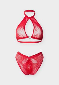 Εσώρουχα από κόκκινη δαντέλα, σουτιέν με halter και ταιριαστά σλιπ με μεταλλικά διακοσμητικά σε σχήμα καρδιάς, παρουσιασμένα σε λευκό φόντο.
