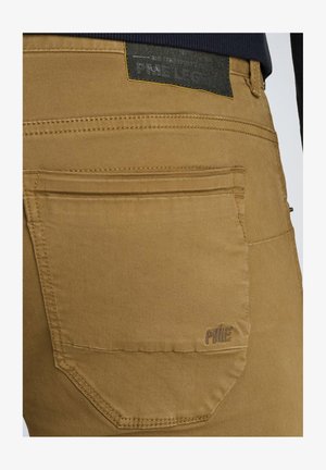 Pantaloni in cotone color sabbia con una tasca posteriore, caratterizzati da cuciture in vista, un'etichetta con logo sopra la tasca e una texture liscia e opaca.