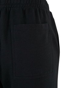 Pantaloni de trening negri cu o textură netedă, talie elastică și un buzunar pătrat pe spate. Design simplu și detalii minime.