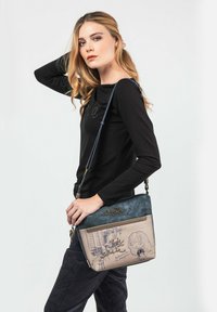 Borsa a tracolla realizzata con materiali misti; presenta un top blu, un corpo beige con un disegno a cartone animato e una tracolla regolabile con accessori in metallo.