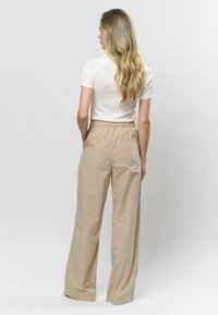 Béžové nohavice so širšími nohavicami a elastickým pásom, s jednou zadnou vreckom, vyrobené z ľahkého materiálu; skombinované s bielym tričkom s krátkym rukávom.