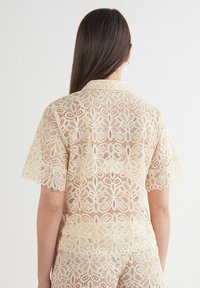 Kanten shirt in crème met een bloempatroon, korte mouwen en een kraag. Textuurstof met een golvende zoom en een open ontwerp.